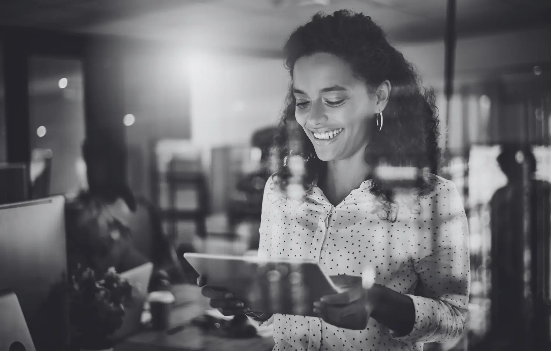 Eine glückliche Geschäftsfrau sitzt lächelnd im Büro vor ihrem Laptop und schaut auf den Bildschirm, Symbolbild für eine Kundin, die mit ihrer Werbeartikel Sonderanfertigung sehr zufrieden ist.