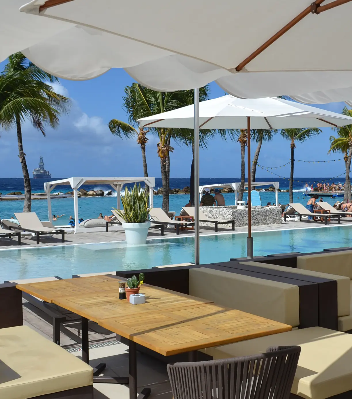 Exklusiver Sommer Beachclub mit Pool, weißen Sonnenschirmen und Lounge-Möbeln direkt am Meer, die ideale Location für den Einsatz von sommerlichen Gastro-Werbeartikeln.