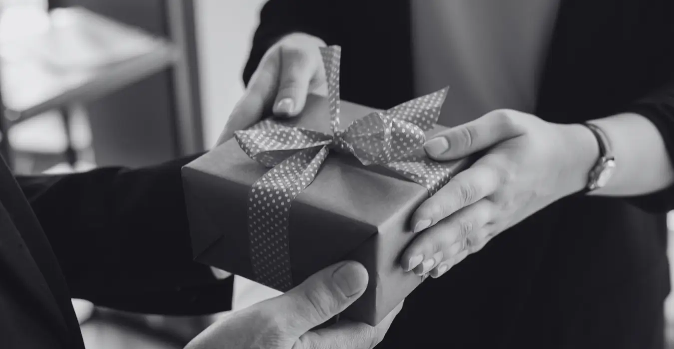Nahaufnahme in Schwarz-Weiß: Eine Person überreicht einer anderen ein Geschenk mit Schleife, Symbolbild für die persönliche Übergabe von Giveaways für Kunden und Geschäftspartner.