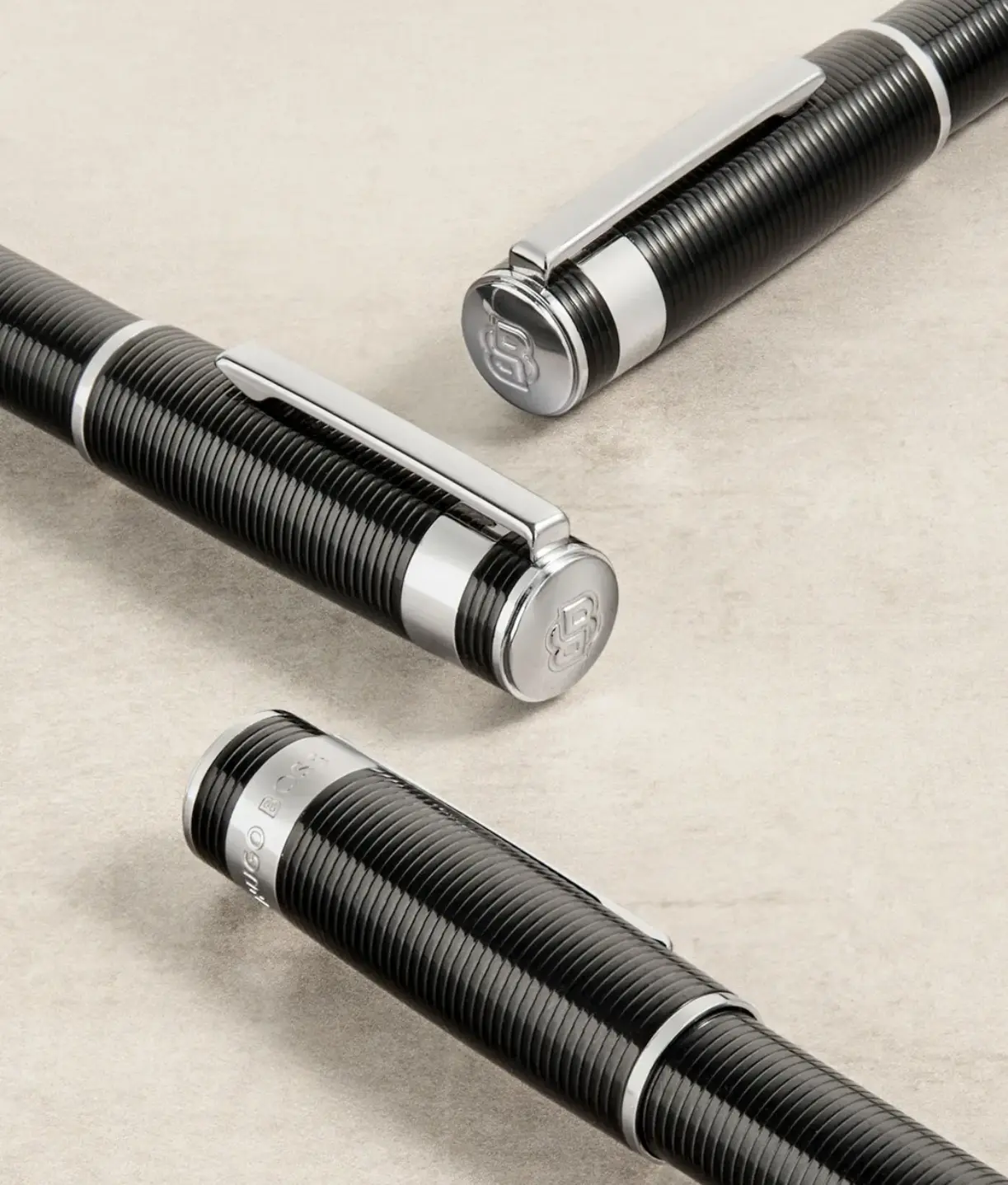 Elegantes Set aus Hugo Boss Schreibgeräten: Schwarze Kugelschreiber mit strukturierter Oberfläche und Chrom-Details auf hellem Untergrund, exklusive Hugo Boss Werbeartikel für Geschäftspartner.