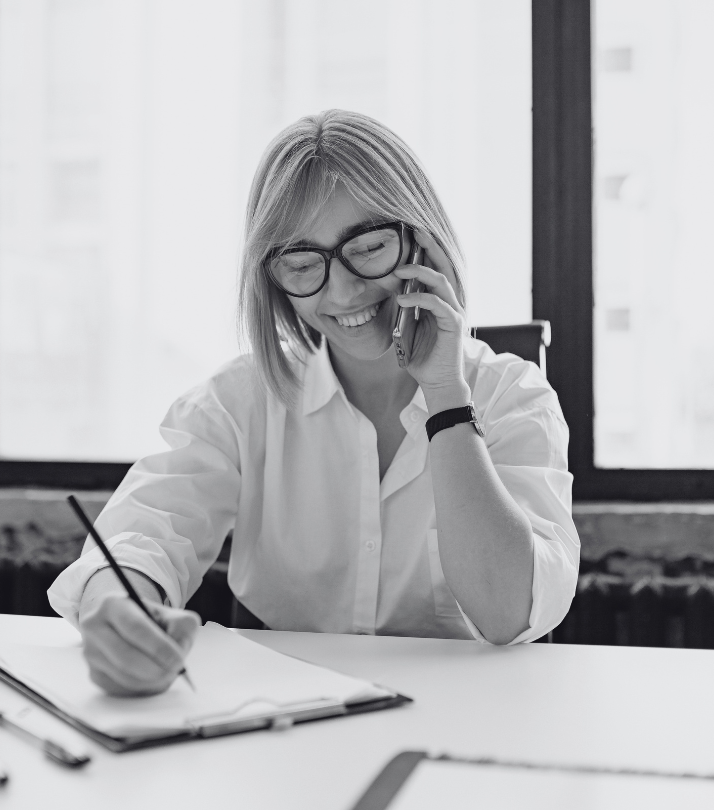 A smiling office professional taking notes on a clipboard while on a call, representing high-quality corporate gifts and office supplies.